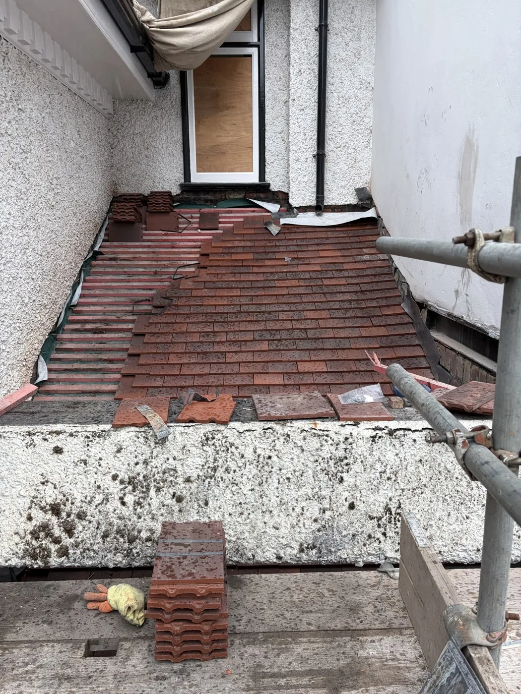 Small red tiles being laid on the porch roof with a section of battens still exposed